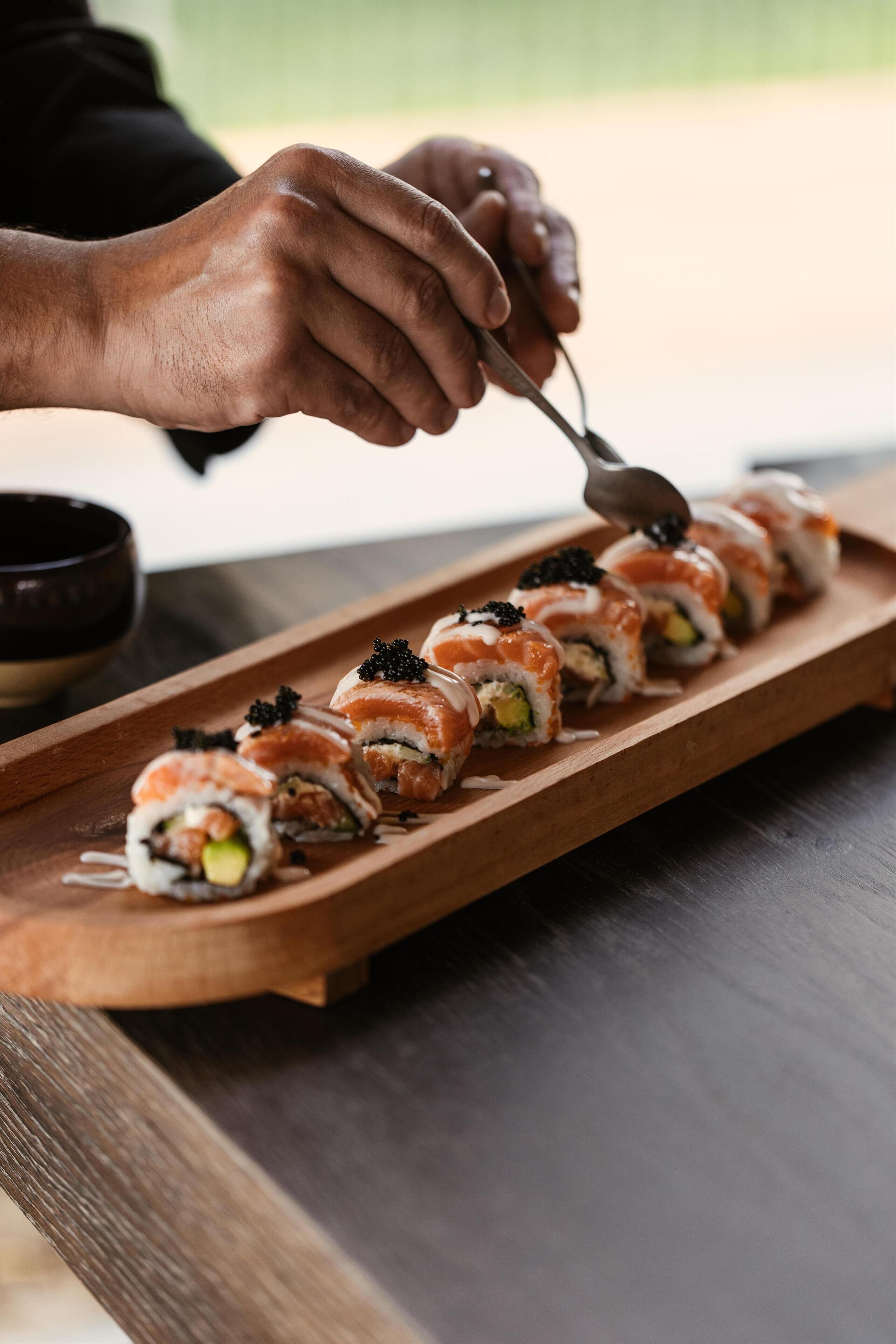 A wooden tray with sushi rolls and a spoon.