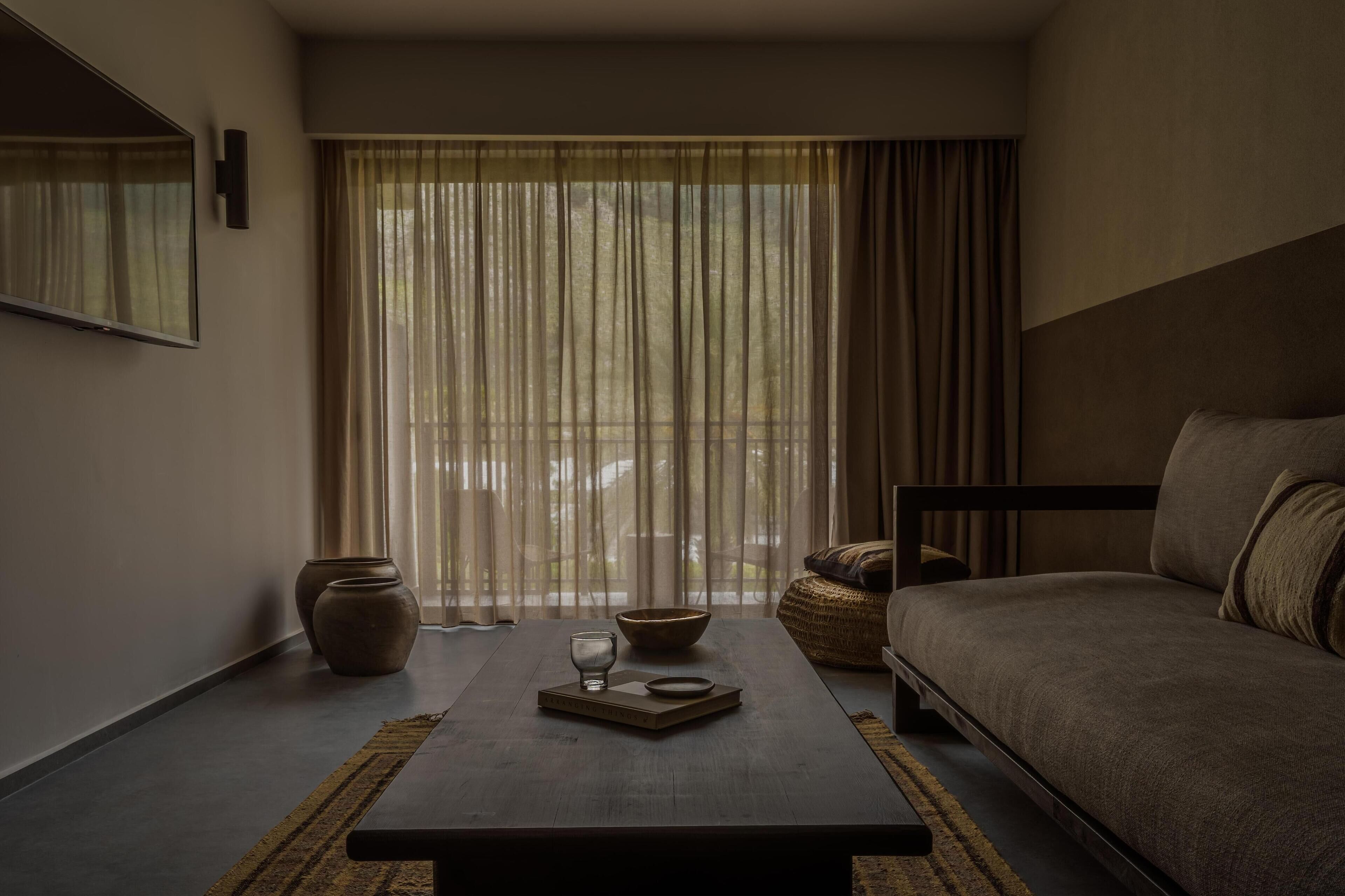 A modern room with a sofa, a coffee table with a bowl and glass, a vase, and sheer curtains.