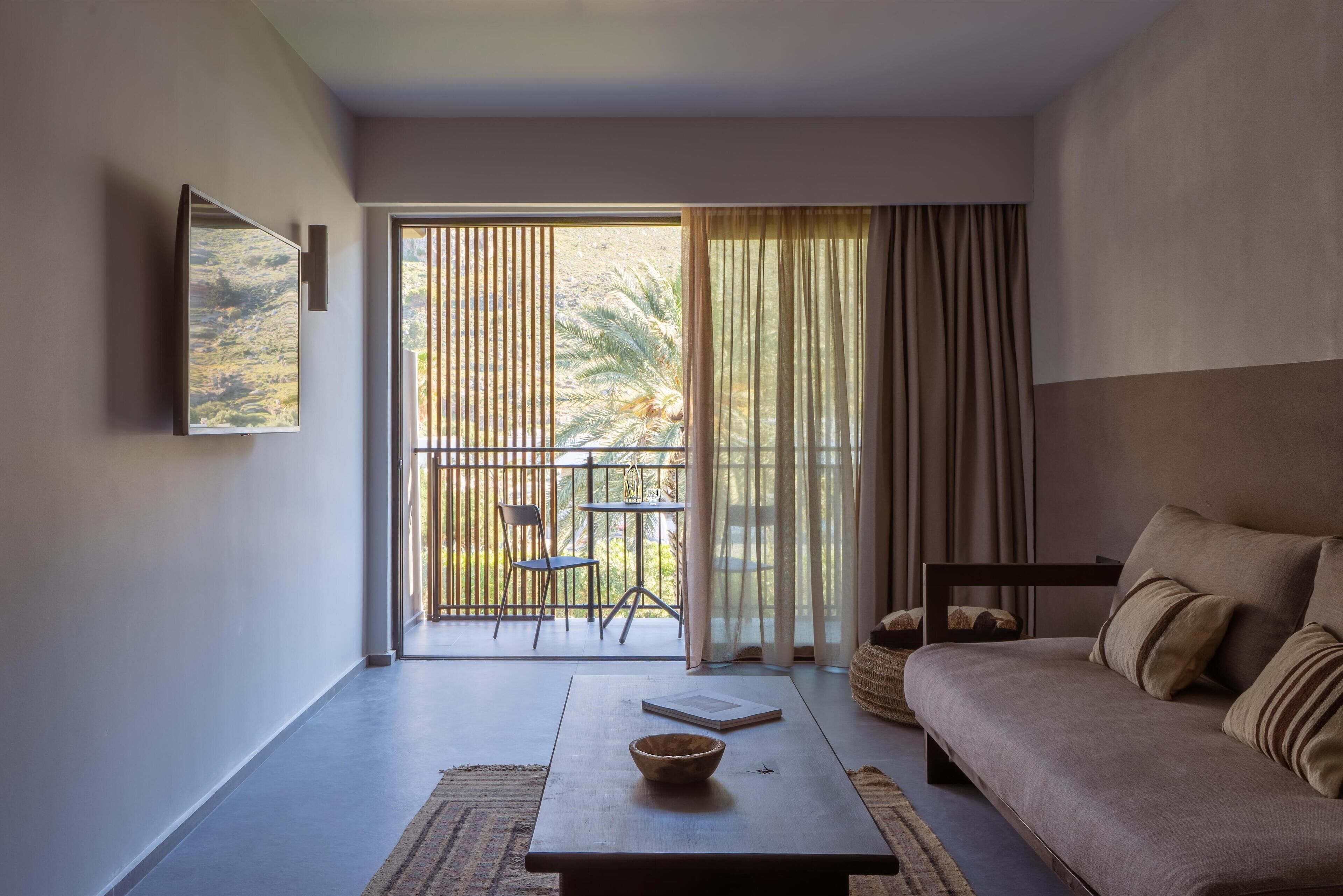 A modern living room with a sofa, a coffee table, and a view of a balcony with outdoor furniture.