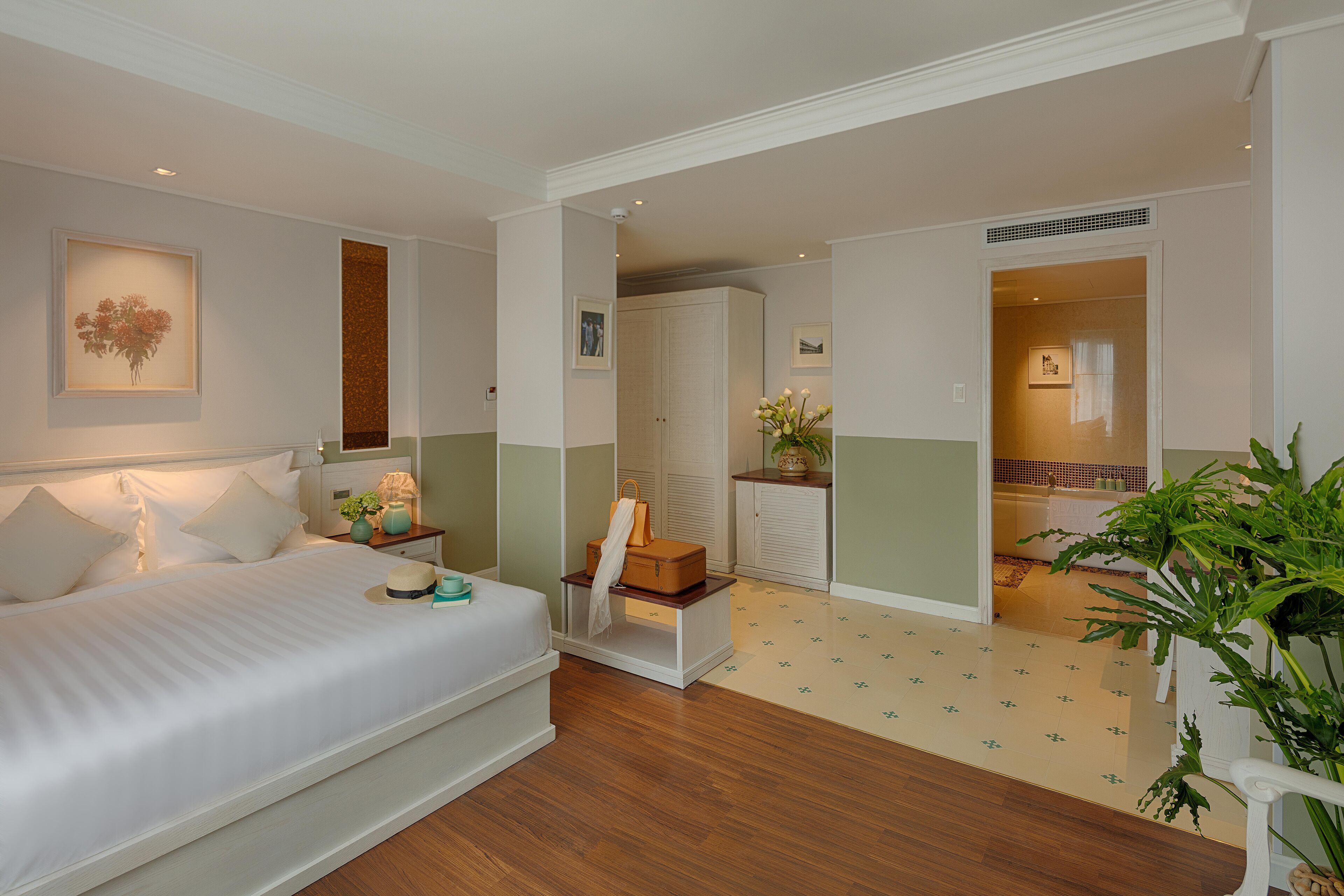 A hotel room with a bed, bedside table, and a small plant.