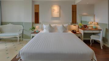 A neatly arranged hotel room with a large bed, a desk with a chair, a small table with a plant, and a mirror.