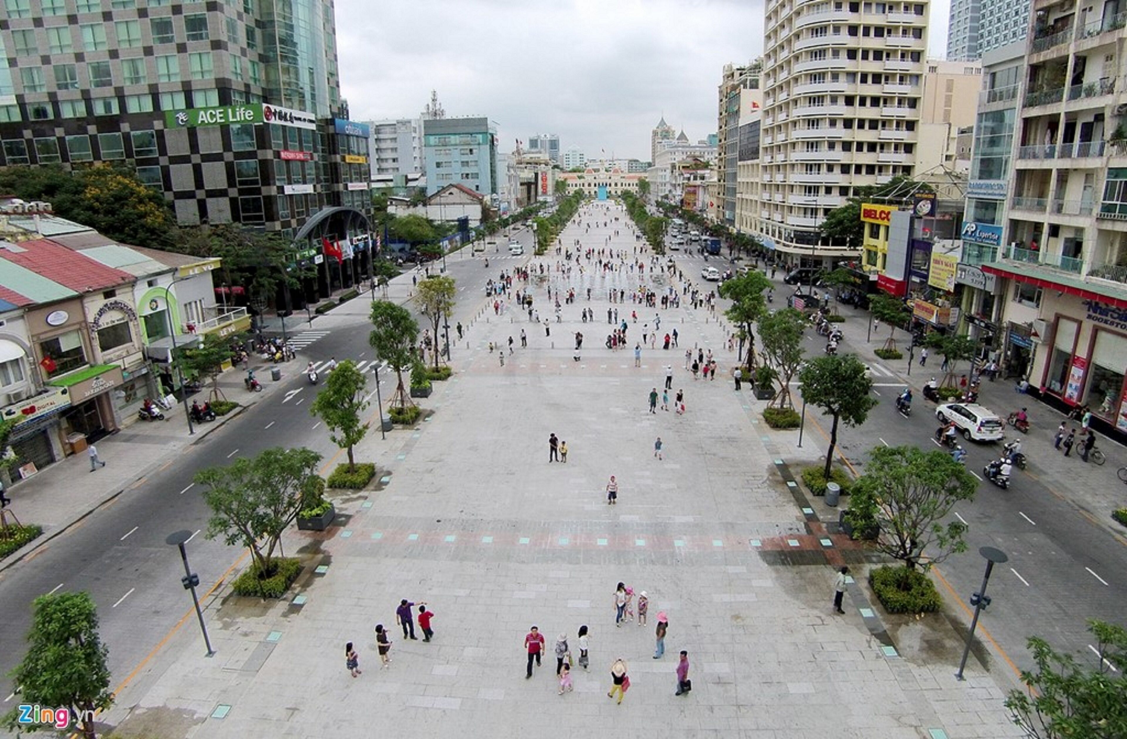 A wide pedestrian plaza with people walking, surrounded by modern buildings and shops.