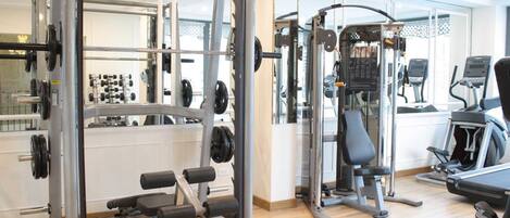 A gym with weightlifting equipment, cardio machines, and a mirror wall.