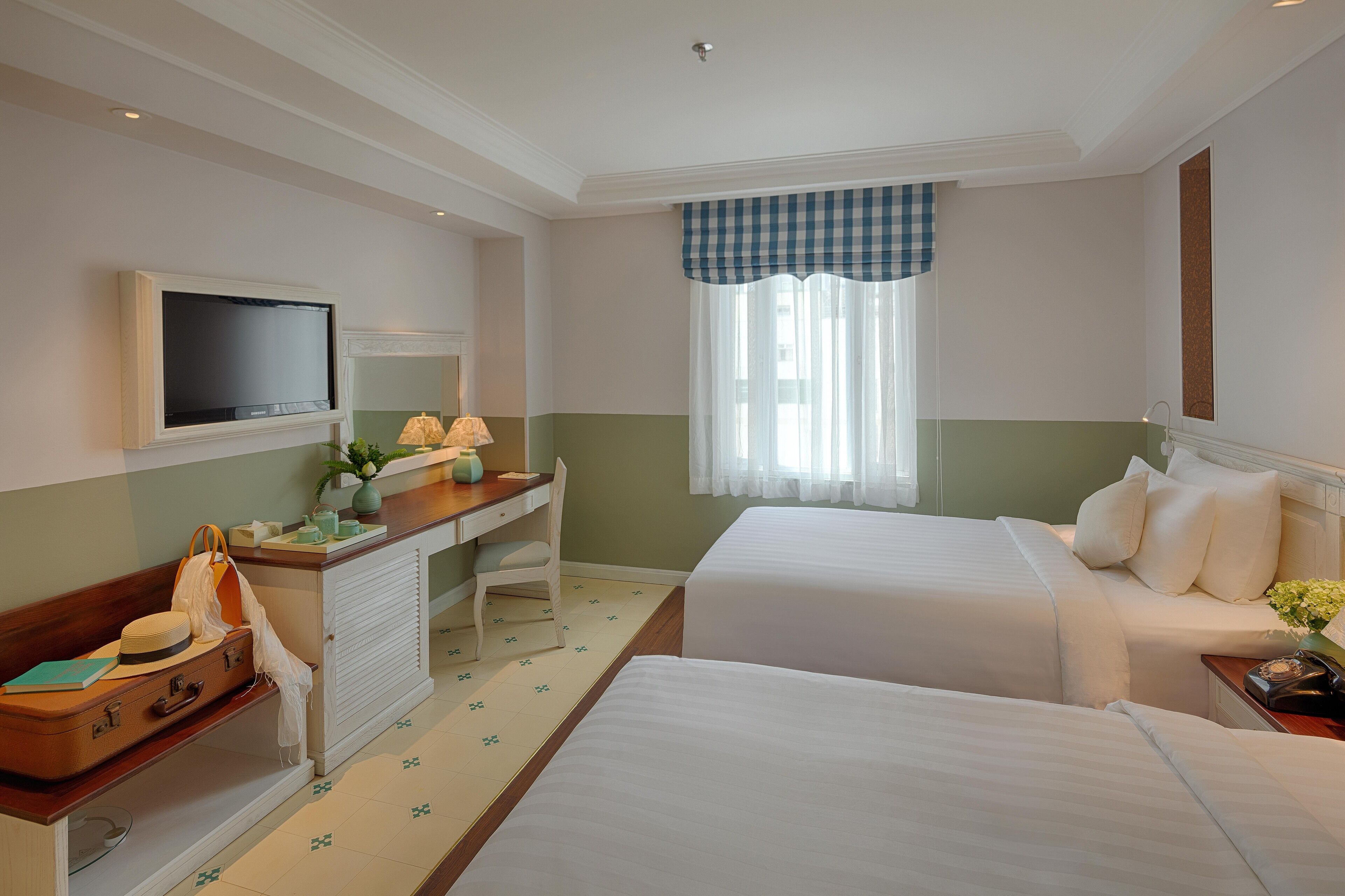 Une chambre d’hôtel avec deux lits, un bureau avec une chaise, une télévision et une fenêtre avec des rideaux.