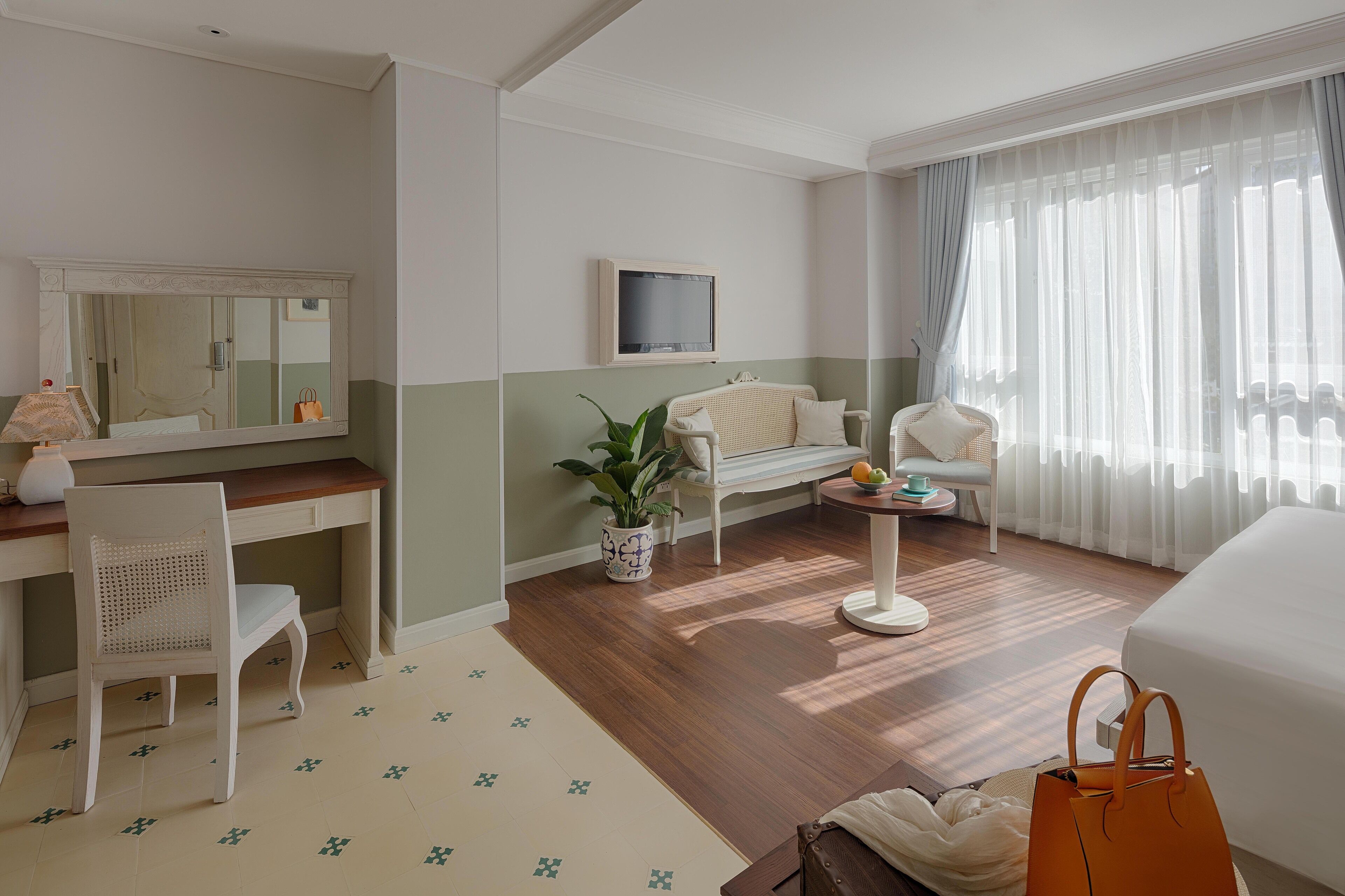 A hotel room with a desk, chair, bed, and a small table with a plant.