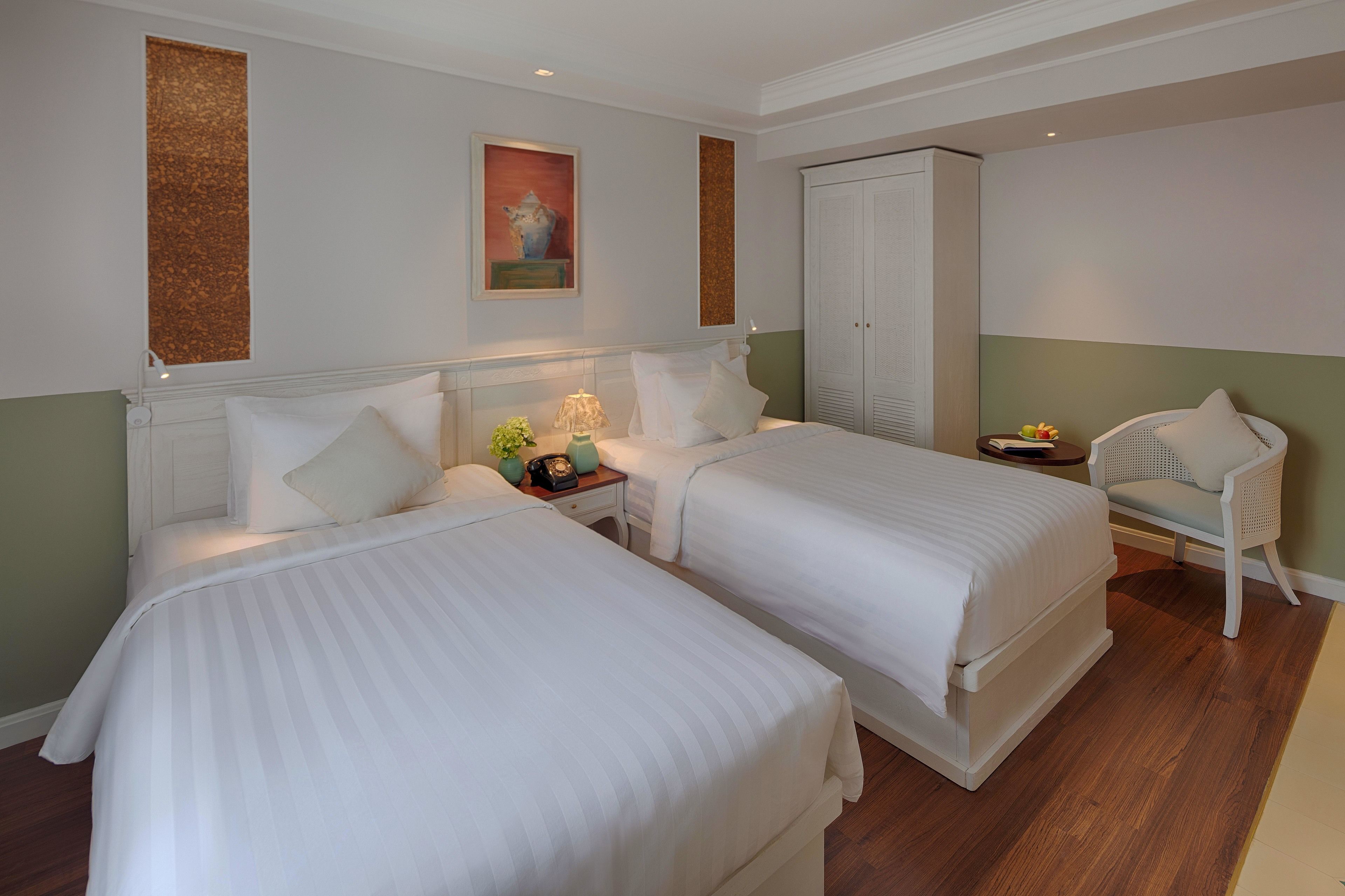 A hotel room with two beds, a nightstand with a lamp, a chair, and a wardrobe.