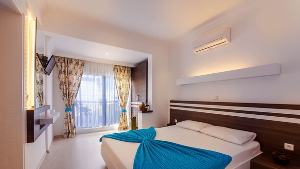 Habitación de hotel con cama, televisor montado en la pared, ventana con cortinas y aire acondicionado.