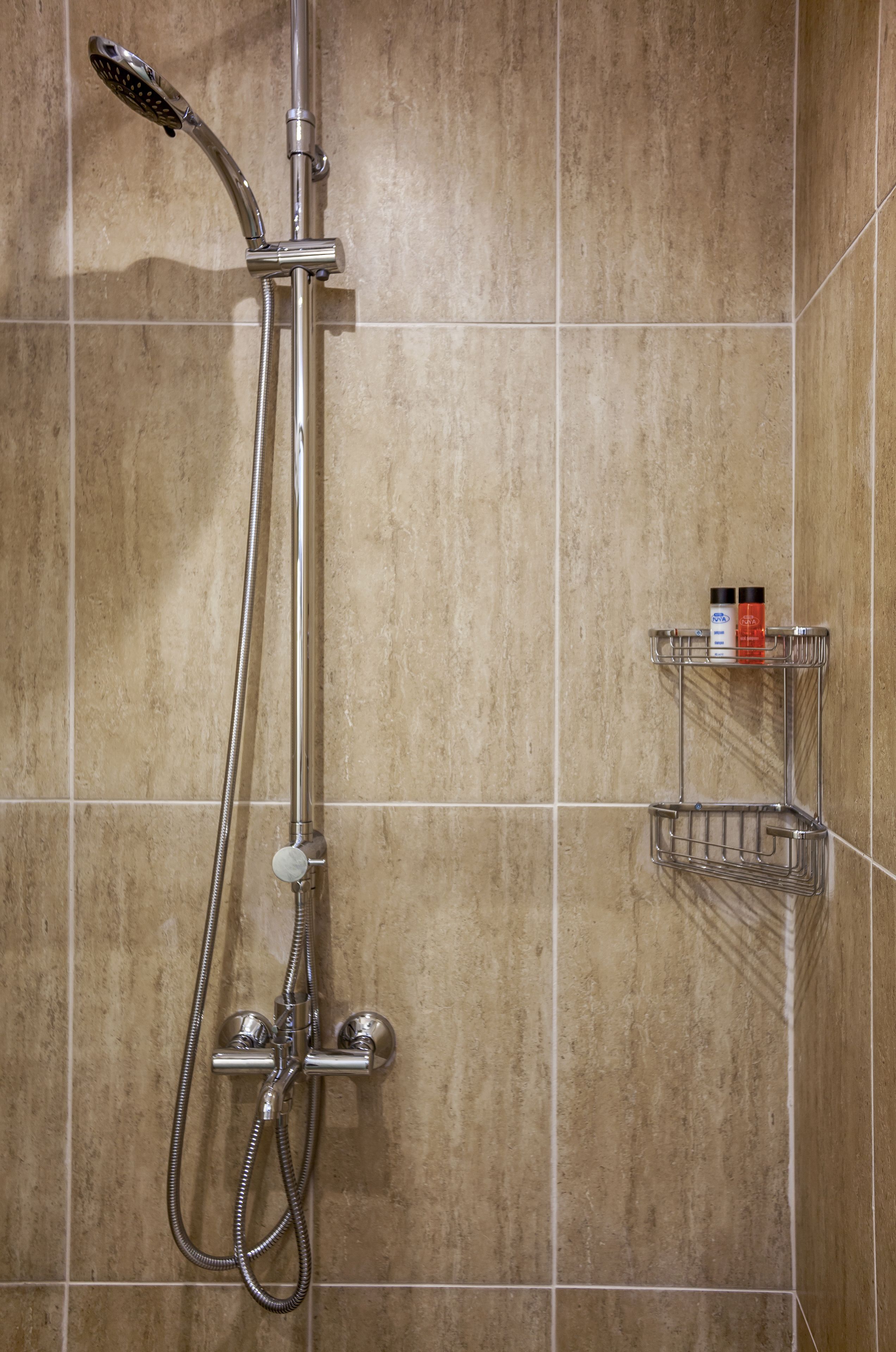 A shower with a handheld showerhead and a wall-mounted faucet, a towel rack, and a small shelf with toiletries.