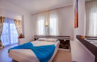 Una habitación de hotel moderna con una cama grande, una mesita de noche, un aparador y una ventana con cortinas.