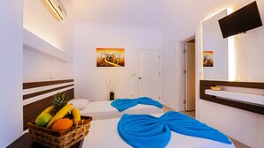 Habitación de hotel con dos camas, una cesta de fruta, un televisor y obras de arte en las paredes.