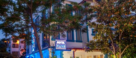 Un hotel con un letrero que dice "HOTEL PUYA", diseño moderno en colores azul y blanco, una escalera que lleva a la entrada y plantas en macetas alrededor del área.