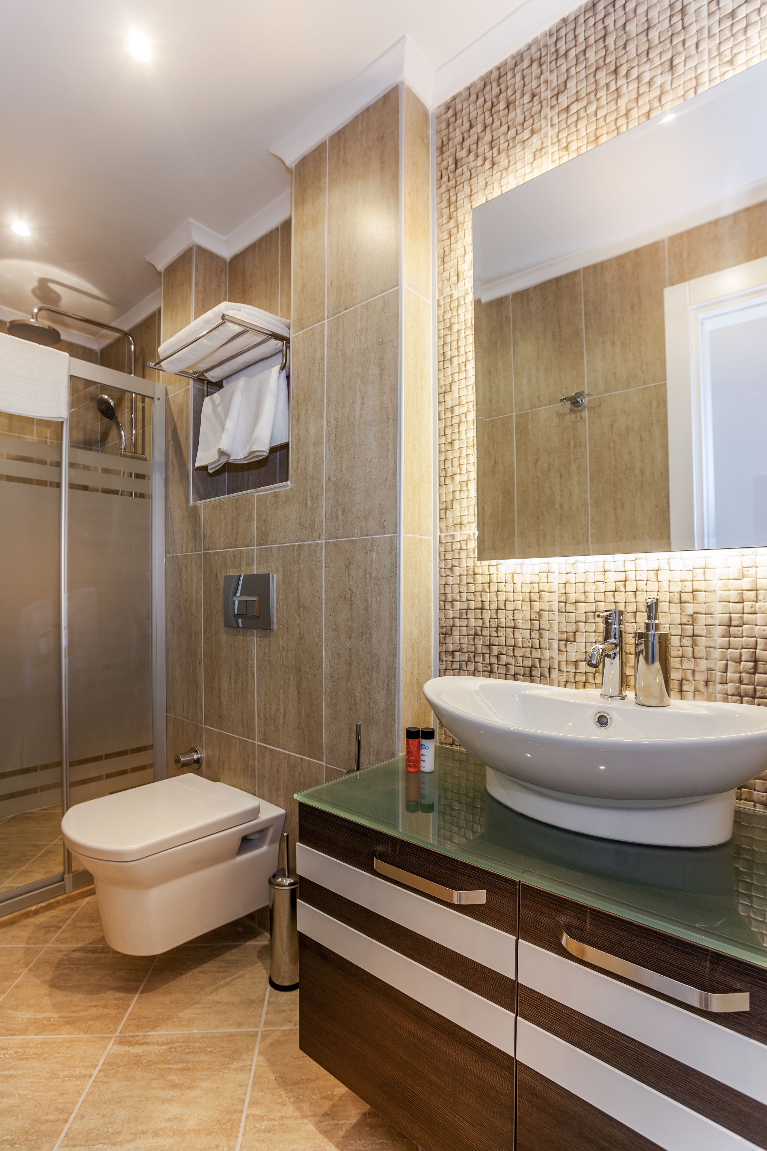A modern bathroom with a glass shower enclosure, a toilet, a sink with a mirror above it, and a towel rack.