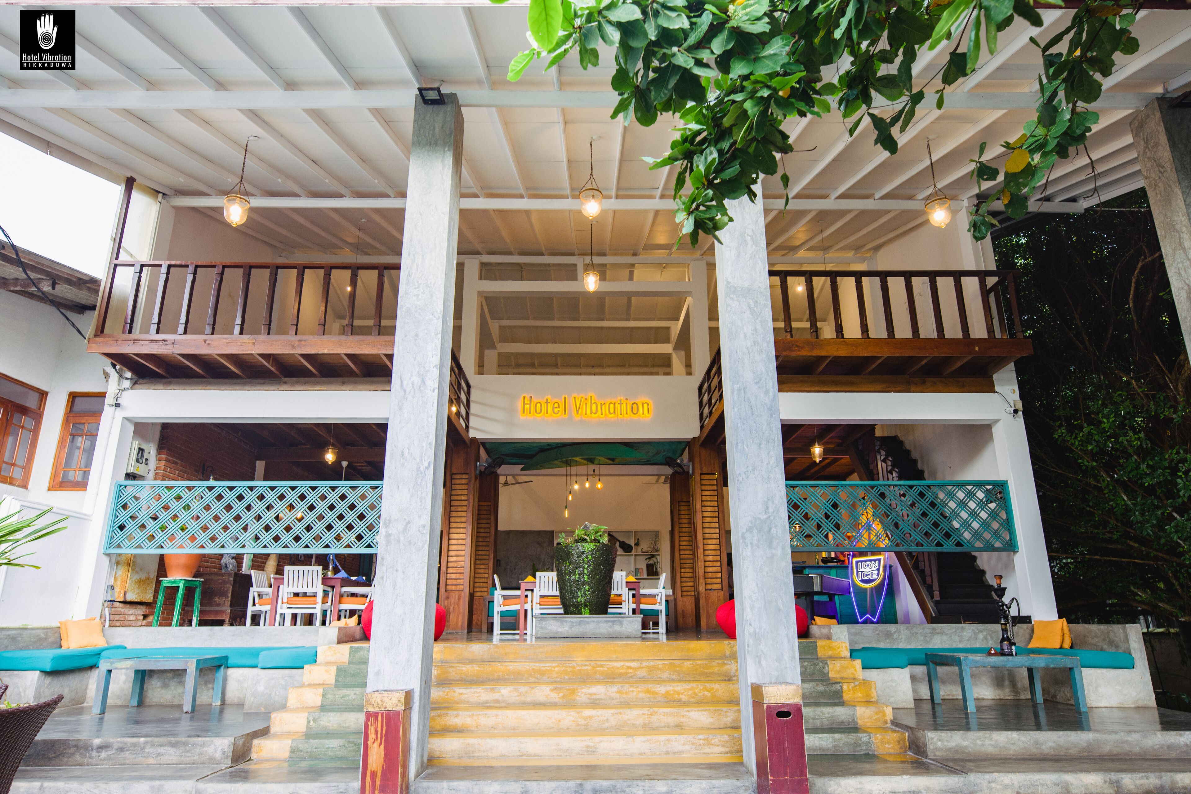 A hotel entrance with a staircase leading to a seating area, a sign reading "Hotel Vibration", and a decorative plant in the center.