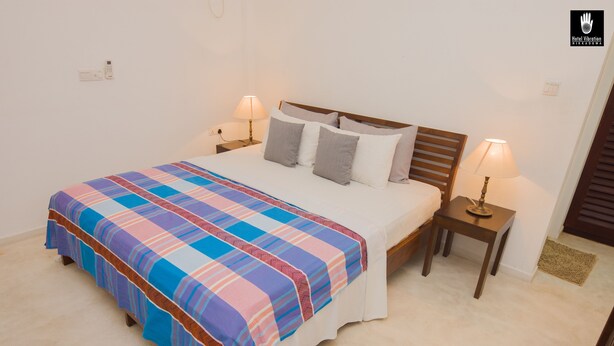 Una cama bien tendida con una colcha a rayas de colores, dos mesitas de noche con lámparas y un cabecero de madera.
