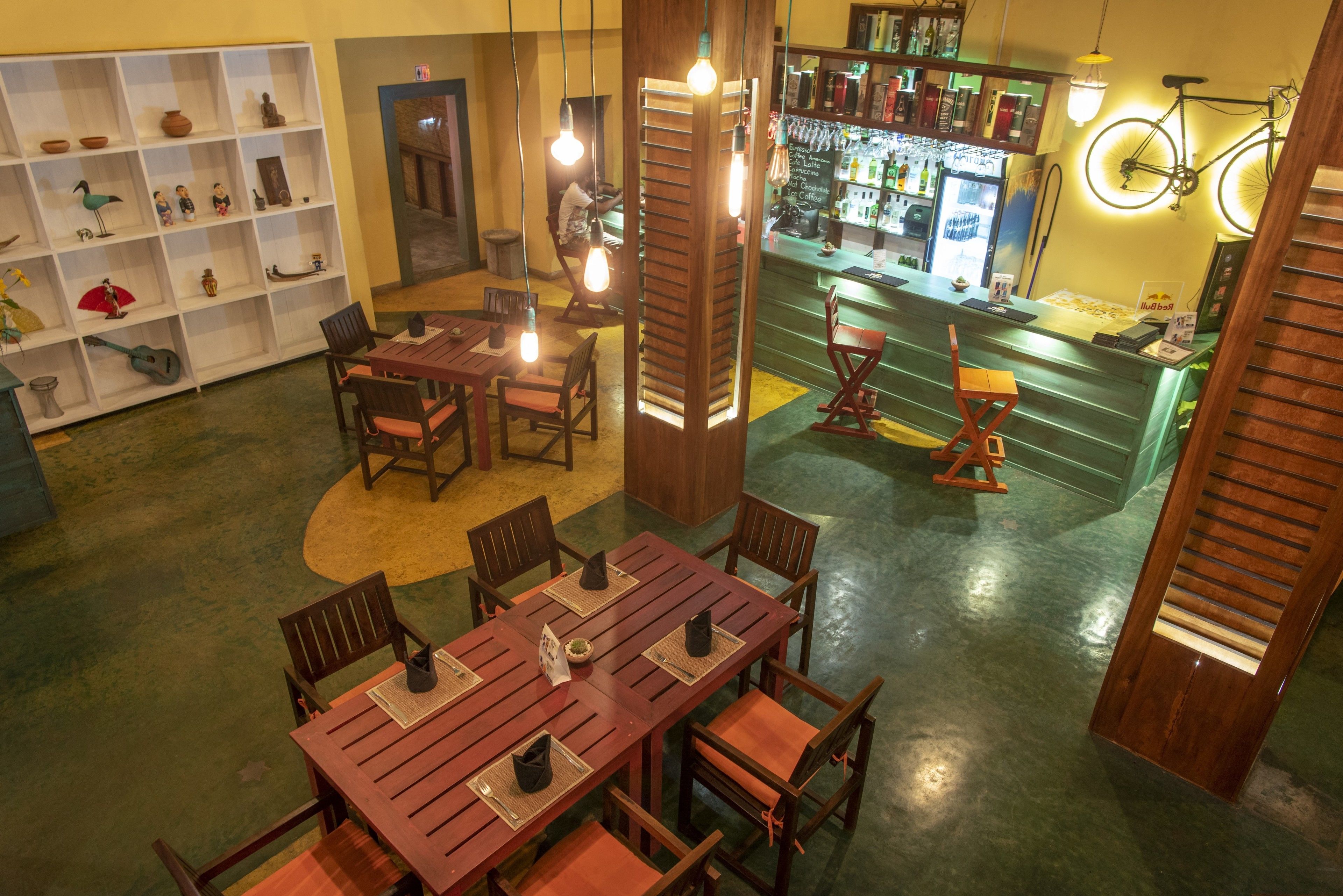 Un restaurant avec des tables et des chaises en bois, un coin bar agrémenté d’un vélo et des étagères remplies de divers objets.