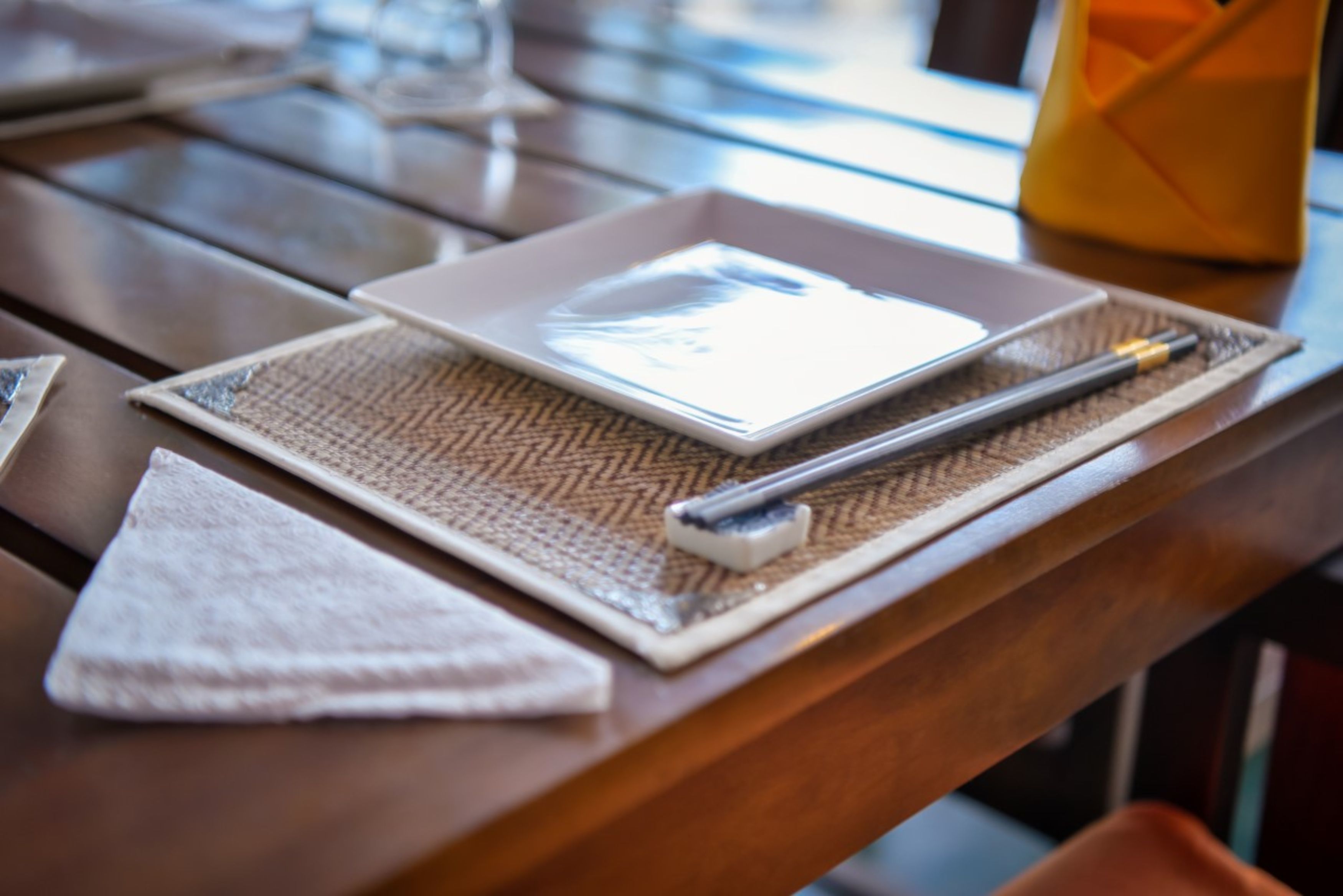 A wooden table with a white placemat, a small white plate, a pen, and a glass of water.