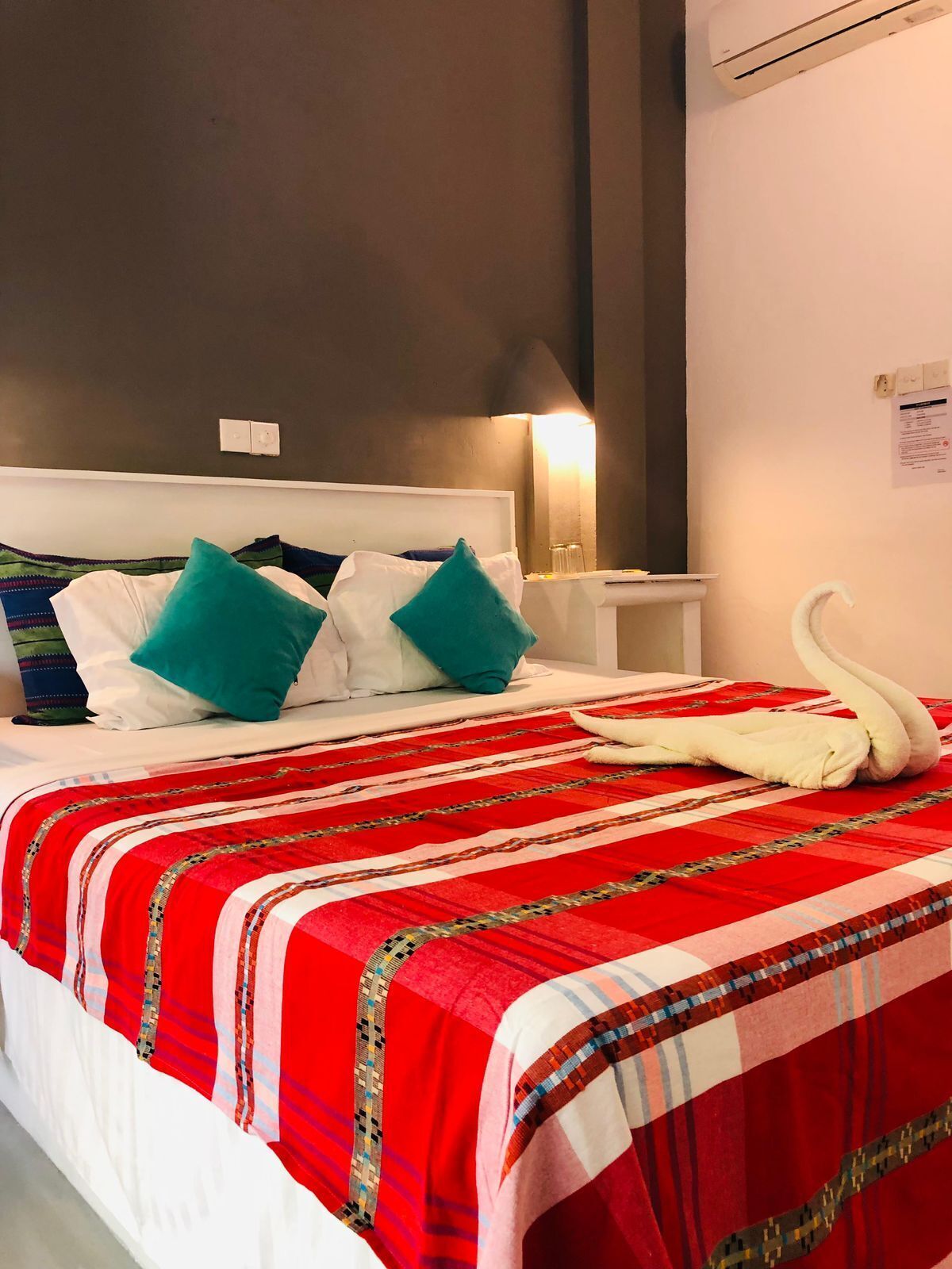A hotel room with a bed, pillows, a swan-shaped towel, and a wall-mounted air conditioner.