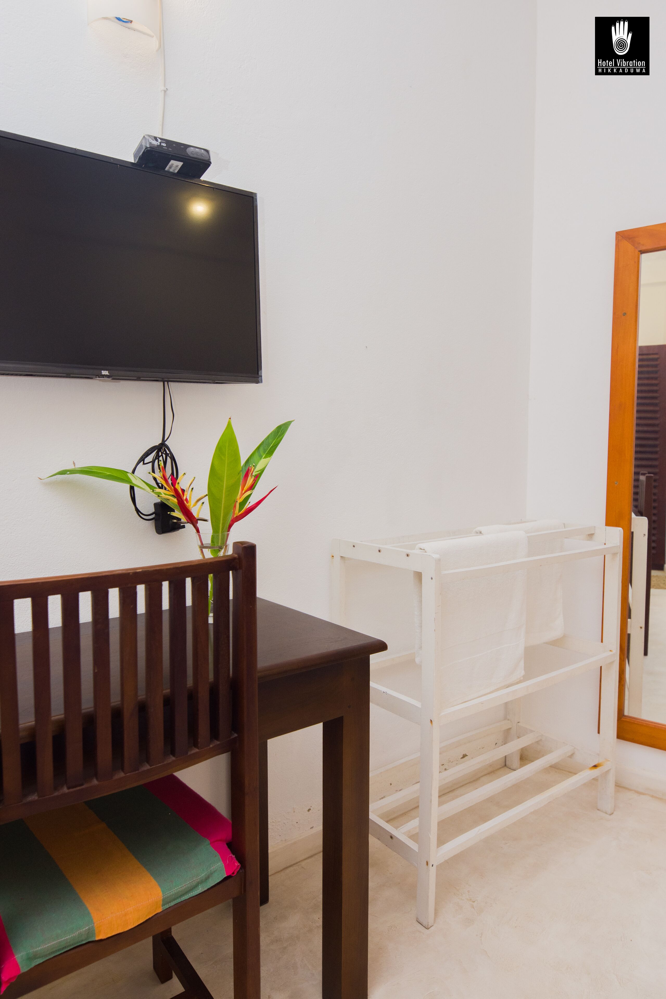 A room with a wooden chair, a white shelf, and a flat-screen TV mounted on the wall.