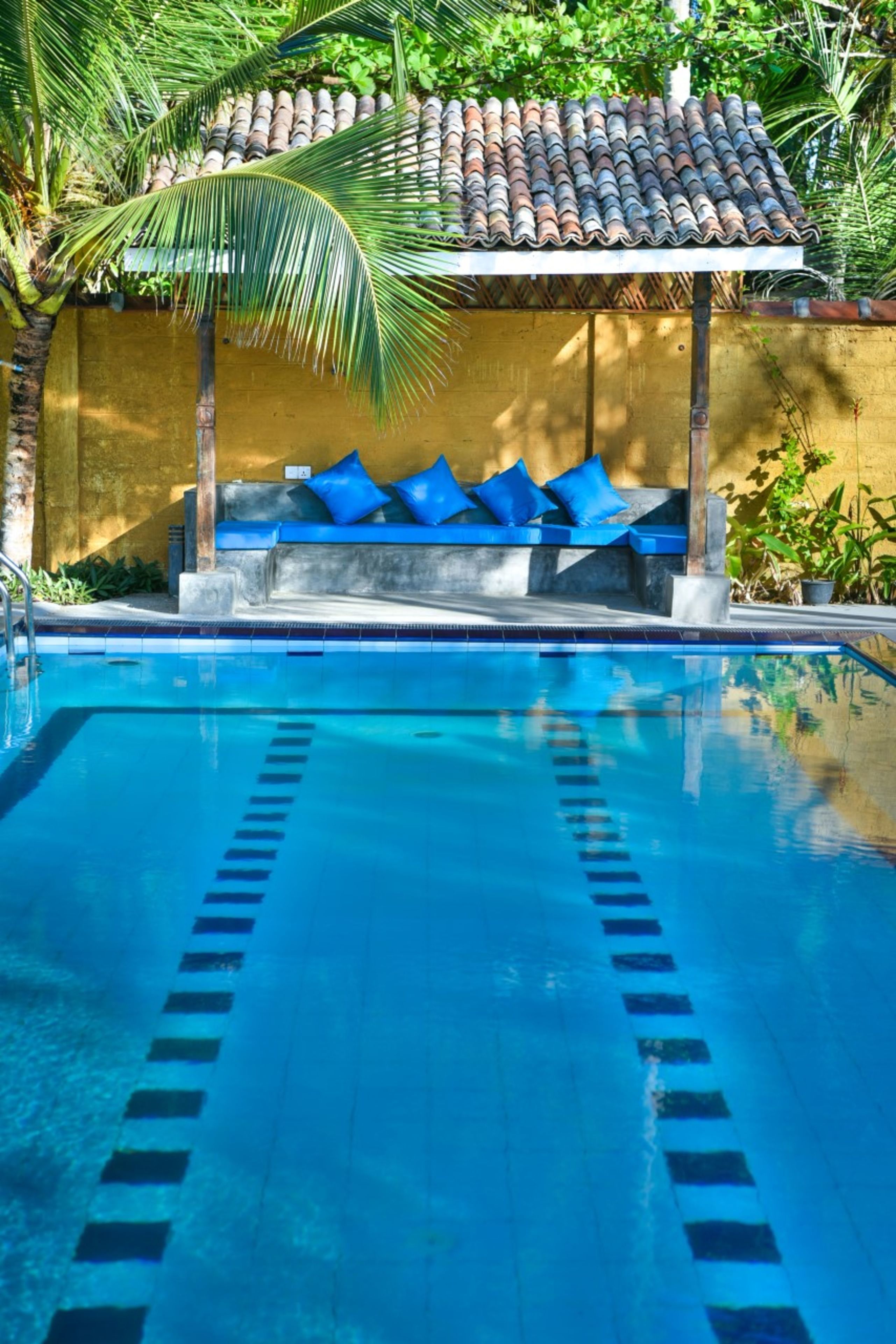 Una piscina con separadores de carril azules, una zona de estar techada con cojines azules y un techo de azulejos.