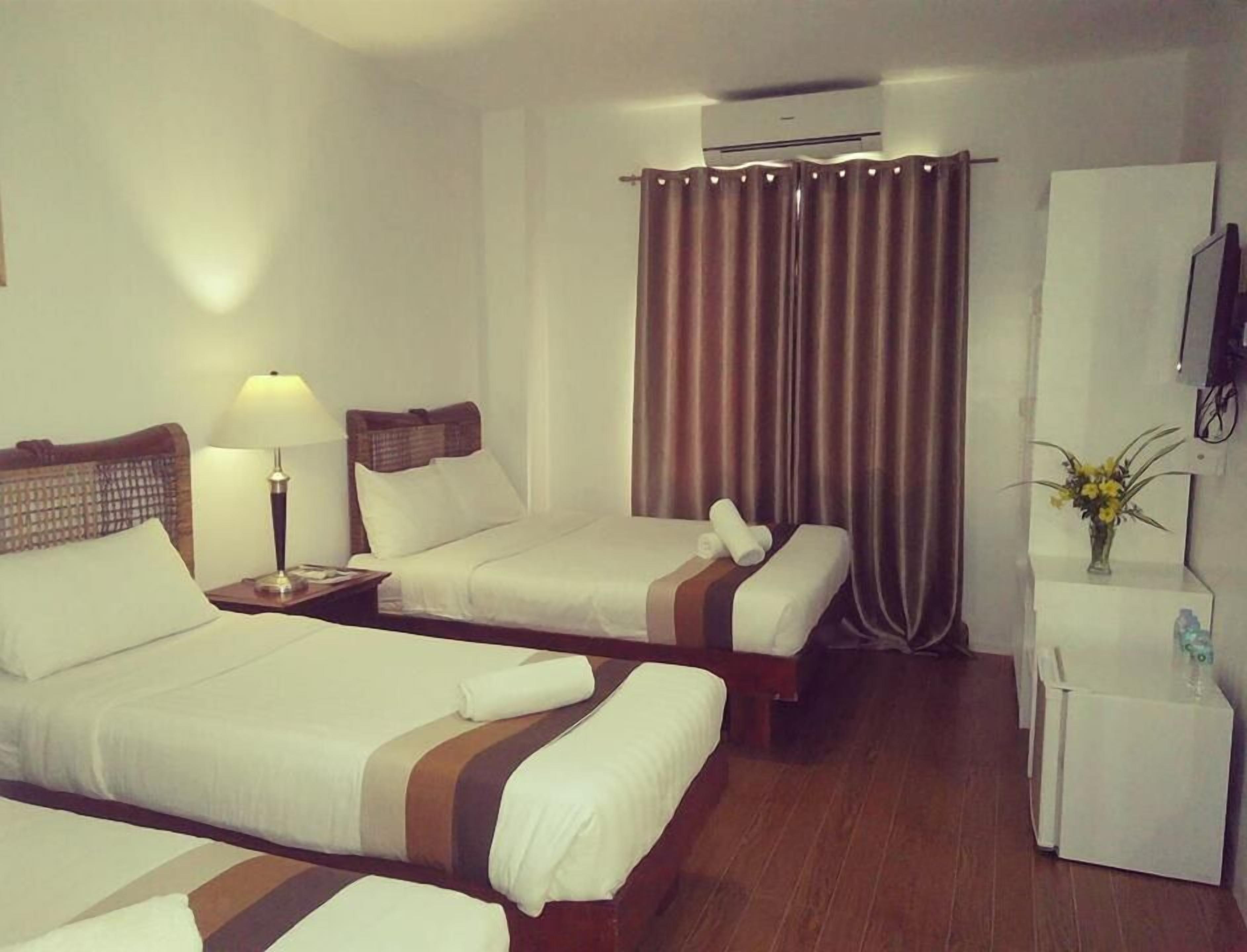 A hotel room with two beds, a desk, a lamp, an air conditioner, and a small refrigerator.