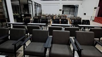 A spacious indoor area with rows of seating, a large table with a marble top, and a high ceiling with recessed lighting.