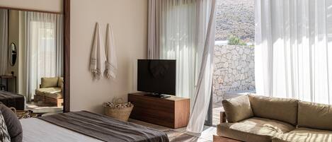 A bedroom with a bed, a sofa, a TV, and a stone wall.