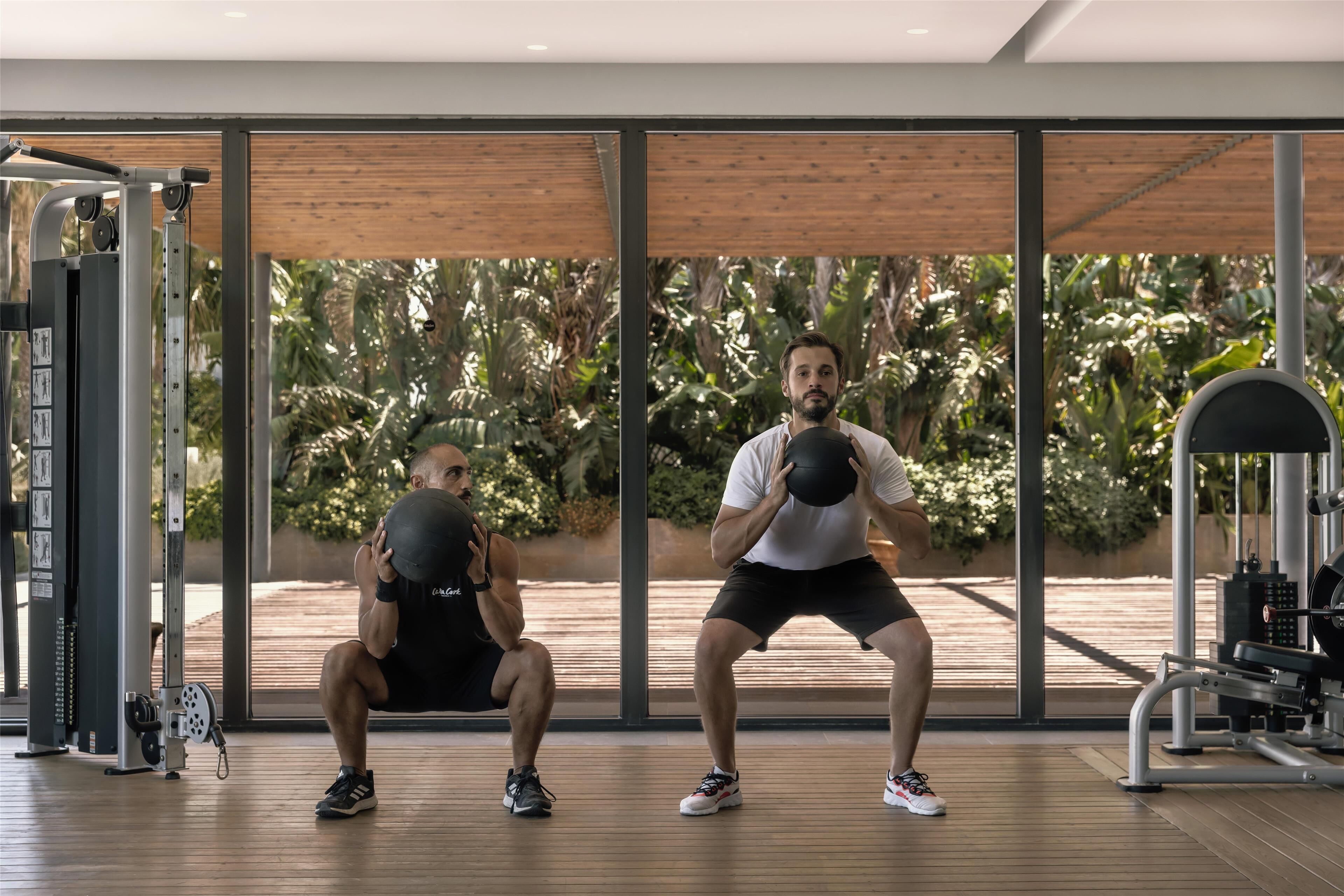 Ein Fitnessraum mit Trainingsgeräten und großen Fenstern mit Blick auf einen Garten.