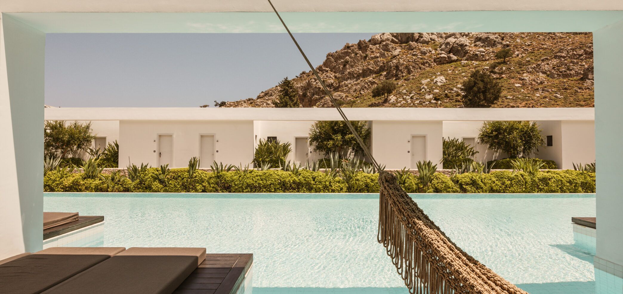 A pool area with lounge chairs, a rope barrier, and a building with multiple doors in the background.