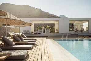 Zona de piscina con sillones reclinables, una terraza de madera y vistas a la montaña.