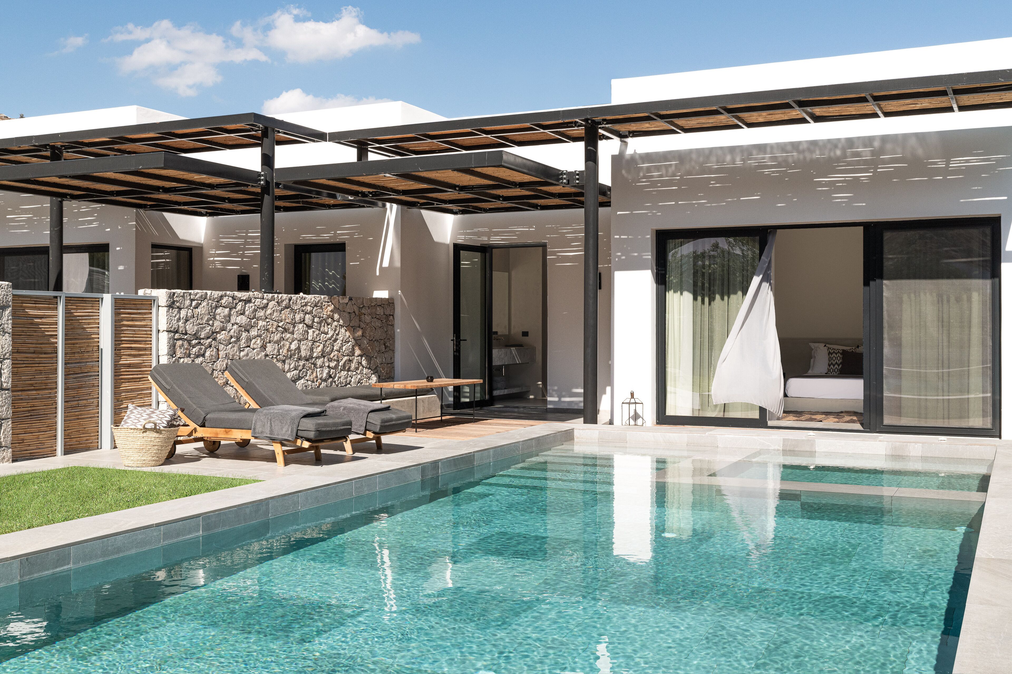 Un área de piscina moderna con una piscina limpia, sillones de descanso y una pared de piedra.
