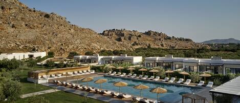 A resort with a large pool, sun loungers, umbrellas, and modern buildings.