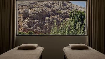 Una habitación con dos camas, un ventanal y vistas a un paisaje rocoso, con cortinas.