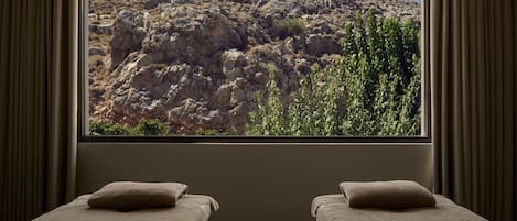 A room with two beds, a large window with a rocky landscape view, and curtains.