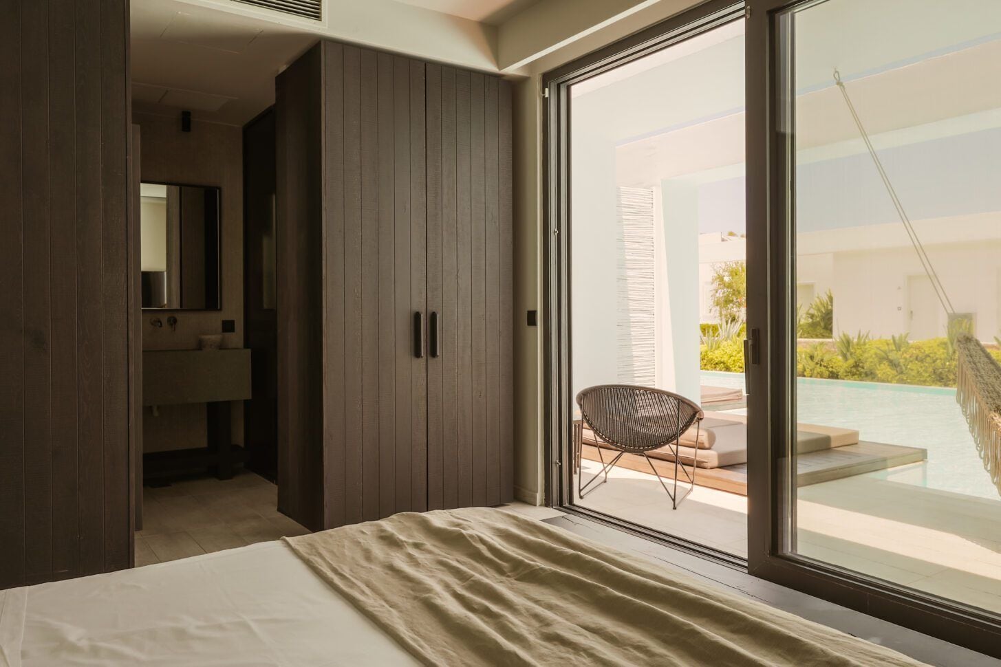 Ein Schlafzimmer mit großem Fenster, einem Bett, einem Sessel und einem Kleiderschrank.