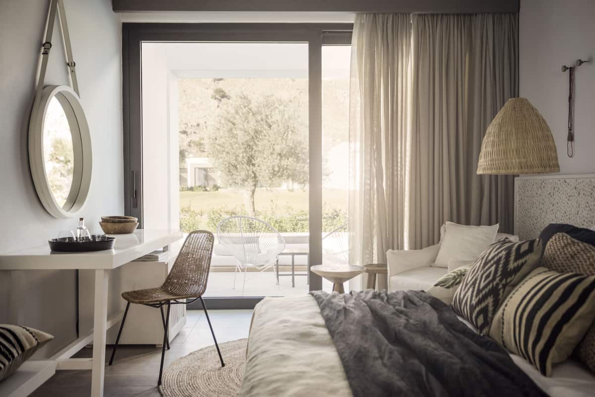 A bedroom with a bed, a desk, a chair, a lamp, and a view of the outdoors.