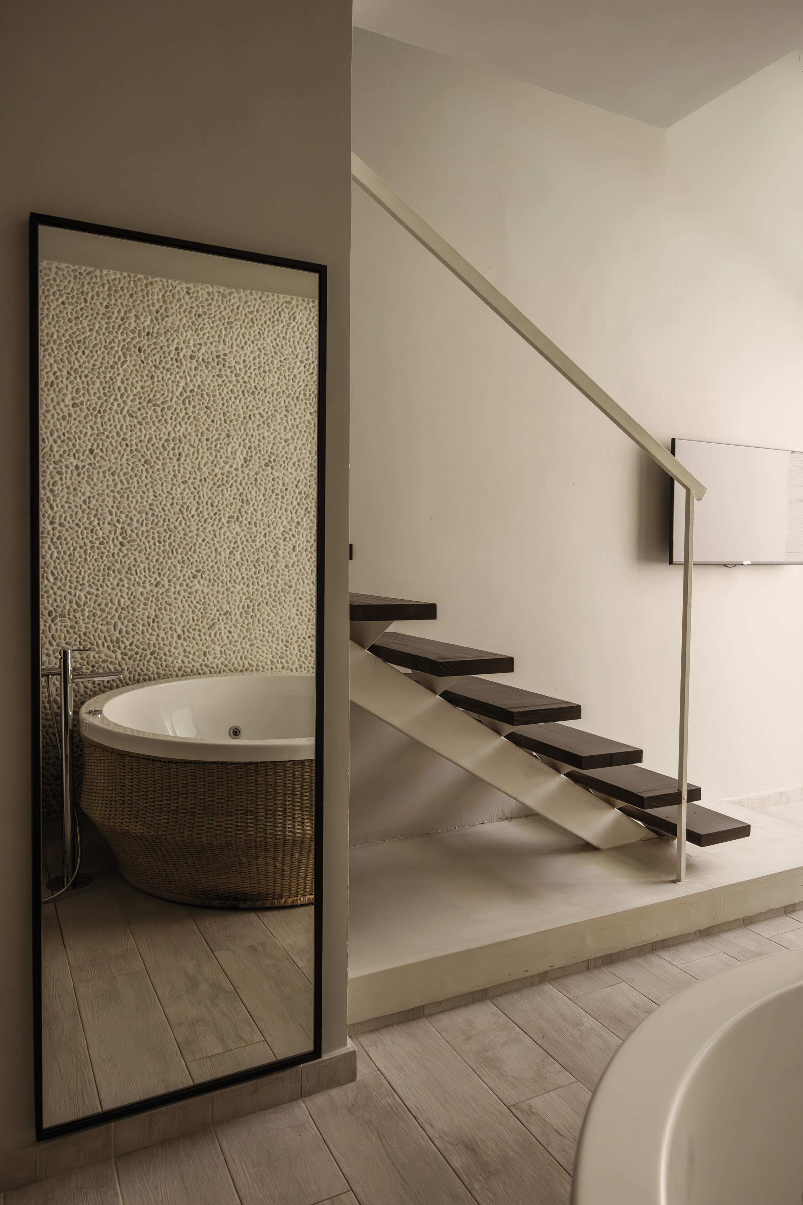 Un baño moderno con una bañera independiente, suelo de madera y una escalera de diseño minimalista.