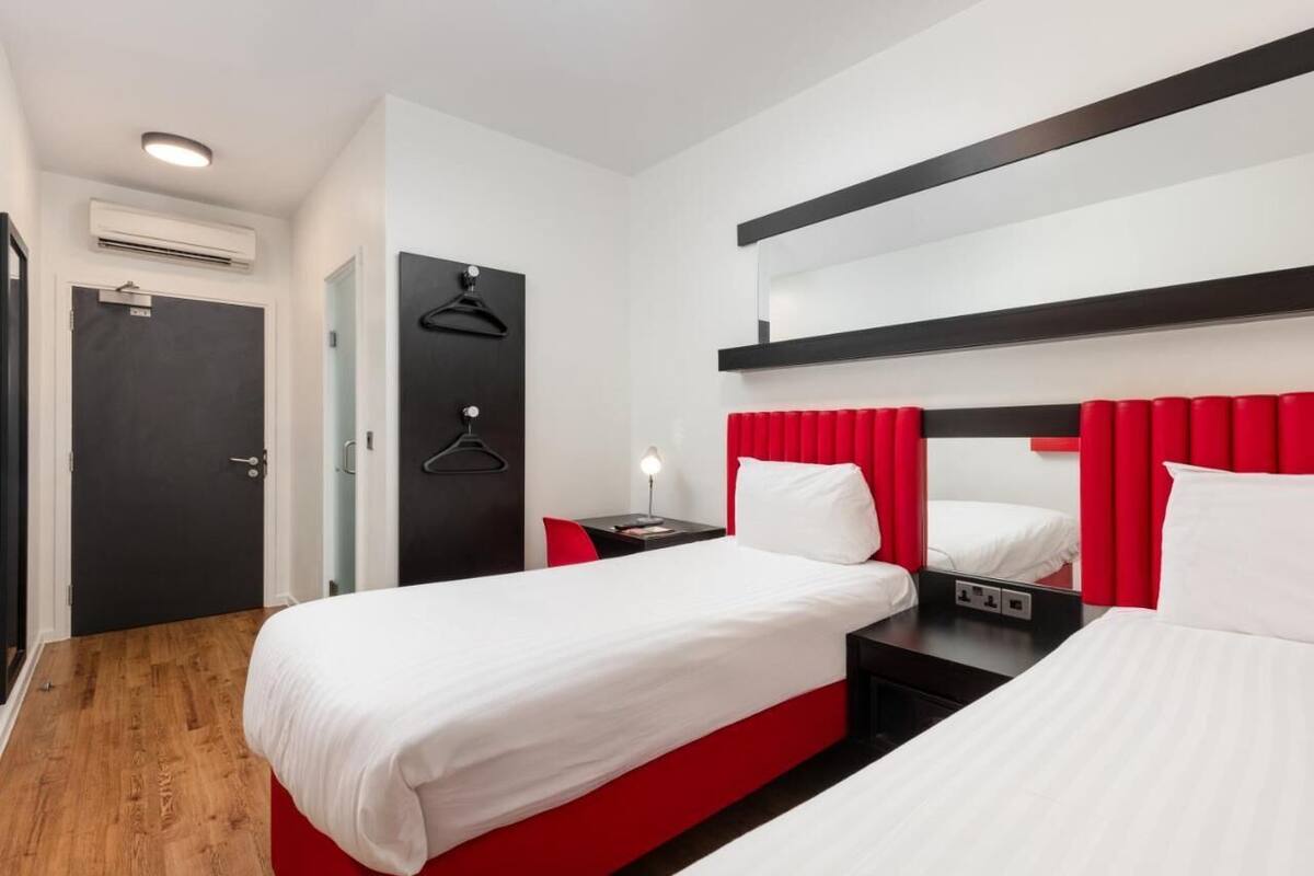 A hotel room with two beds, a black door, a mirror, and a red accent wall.