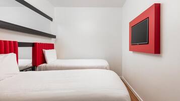 Habitación de hotel con dos camas, una pared de acento roja y un televisor montado.