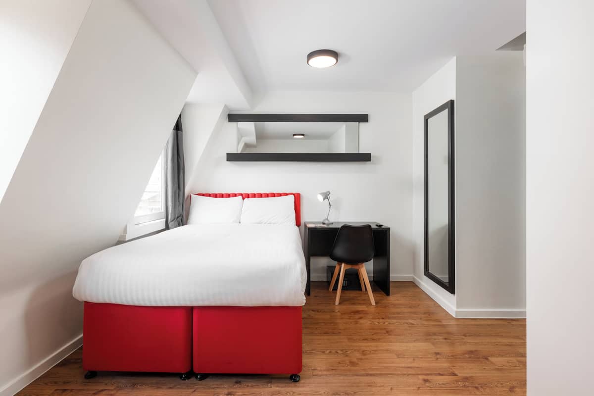 A bedroom with a red bed, a desk, and a chair.