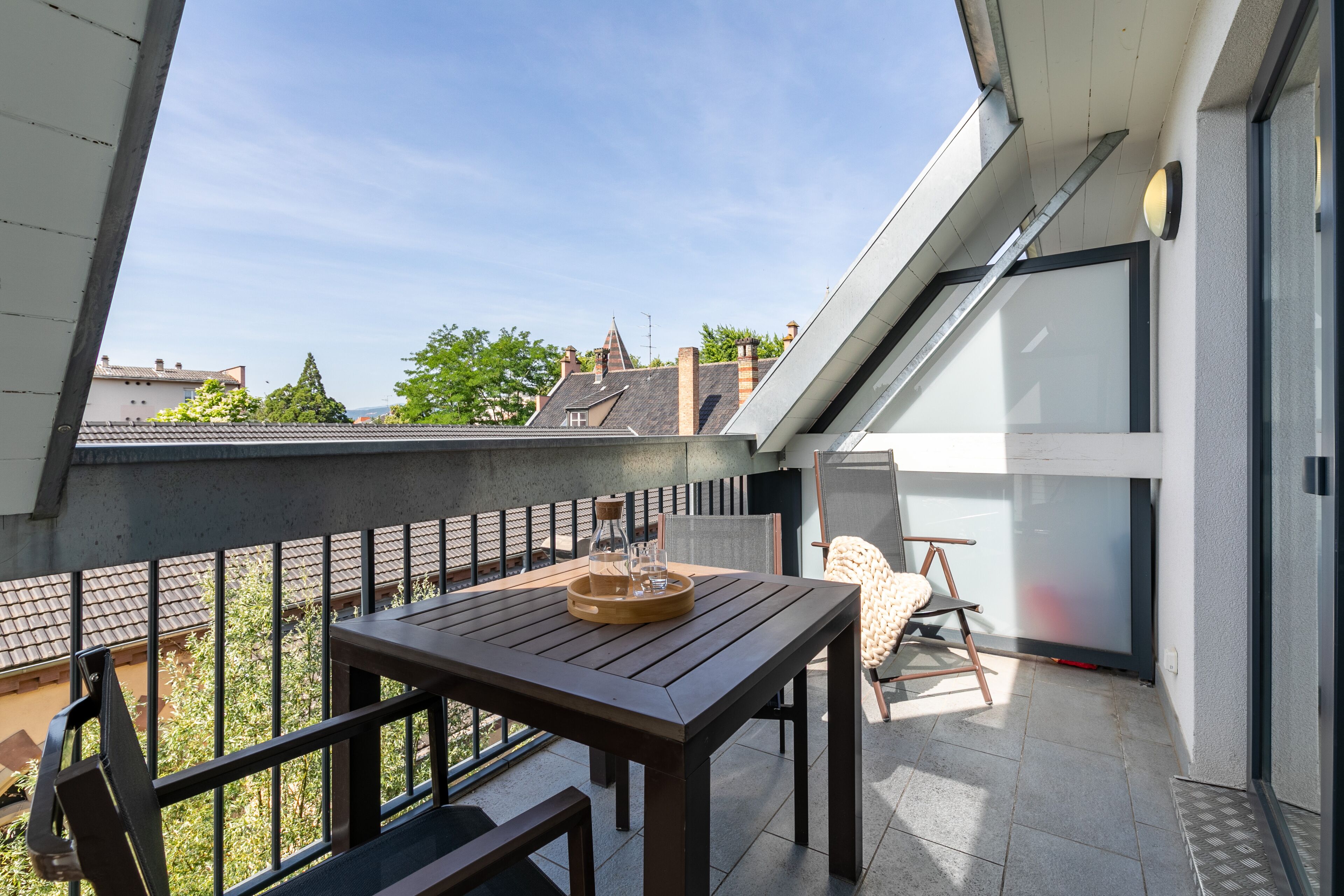 A modern balcony with a wooden table, a chair, and a glass container.