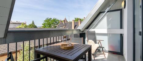 A modern balcony with a wooden table, a chair, and a glass container.