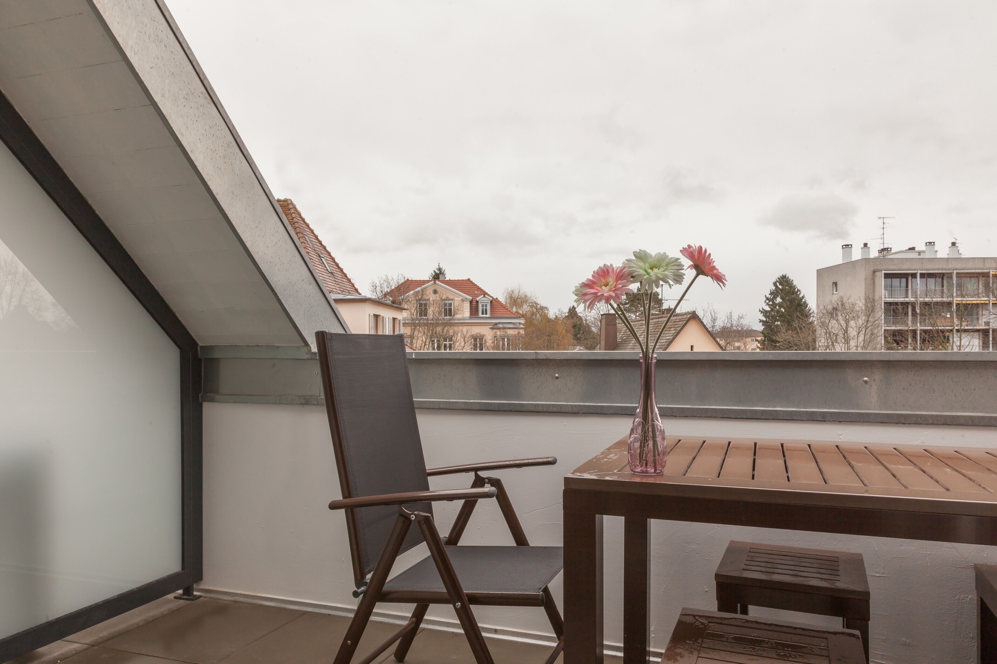 A balcony with a chair, a small table, and a vase with flowers.