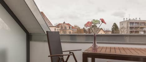 A balcony with a chair, a small table, and a vase with flowers.