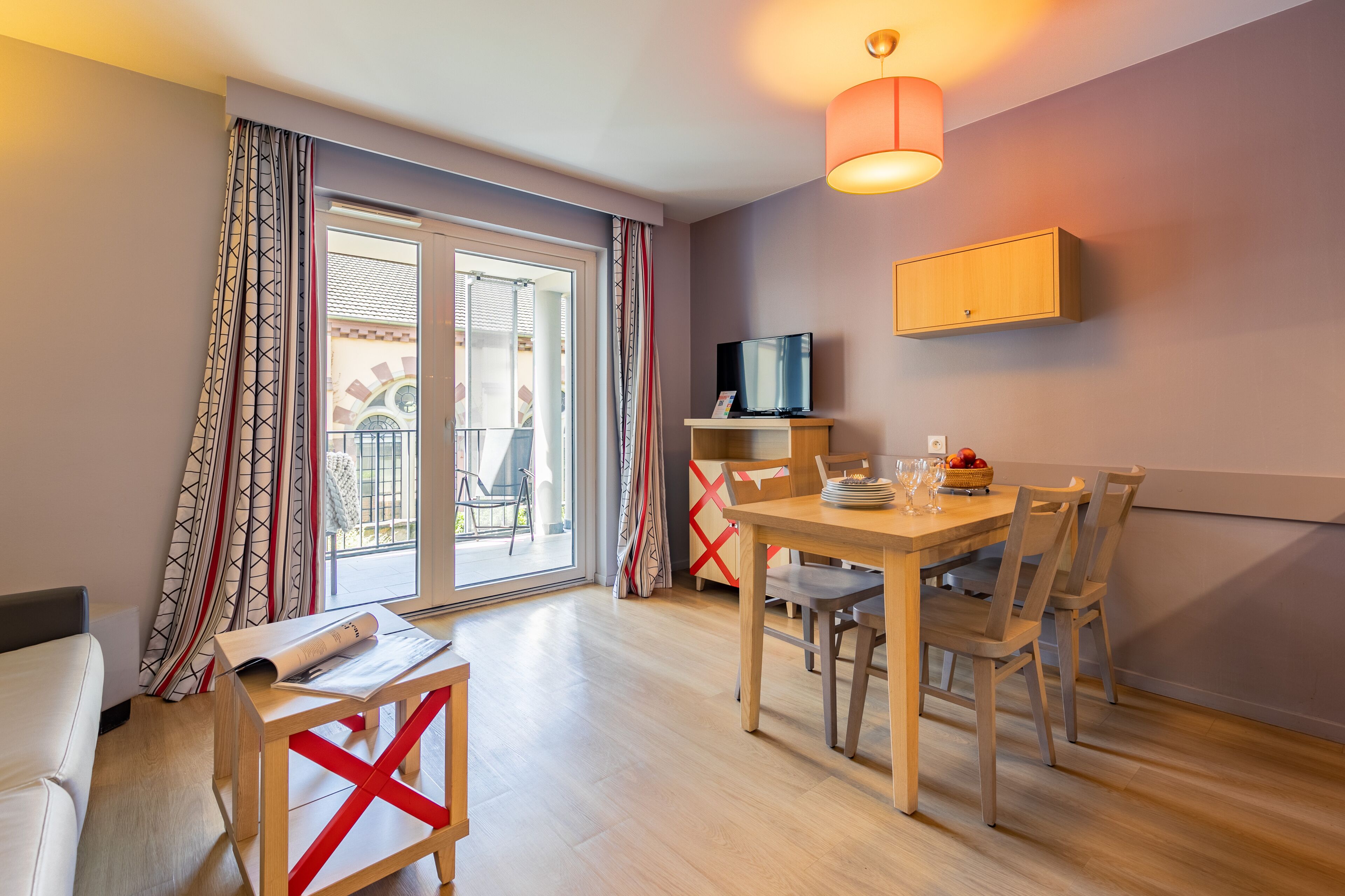 Un salon moderne avec un canapé, une table à manger et des chaises, un téléviseur posé sur un meuble et un balcon avec vue.