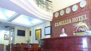 A reception desk at Camellia Hotel with a clock, a reception sign, and a floral arrangement.