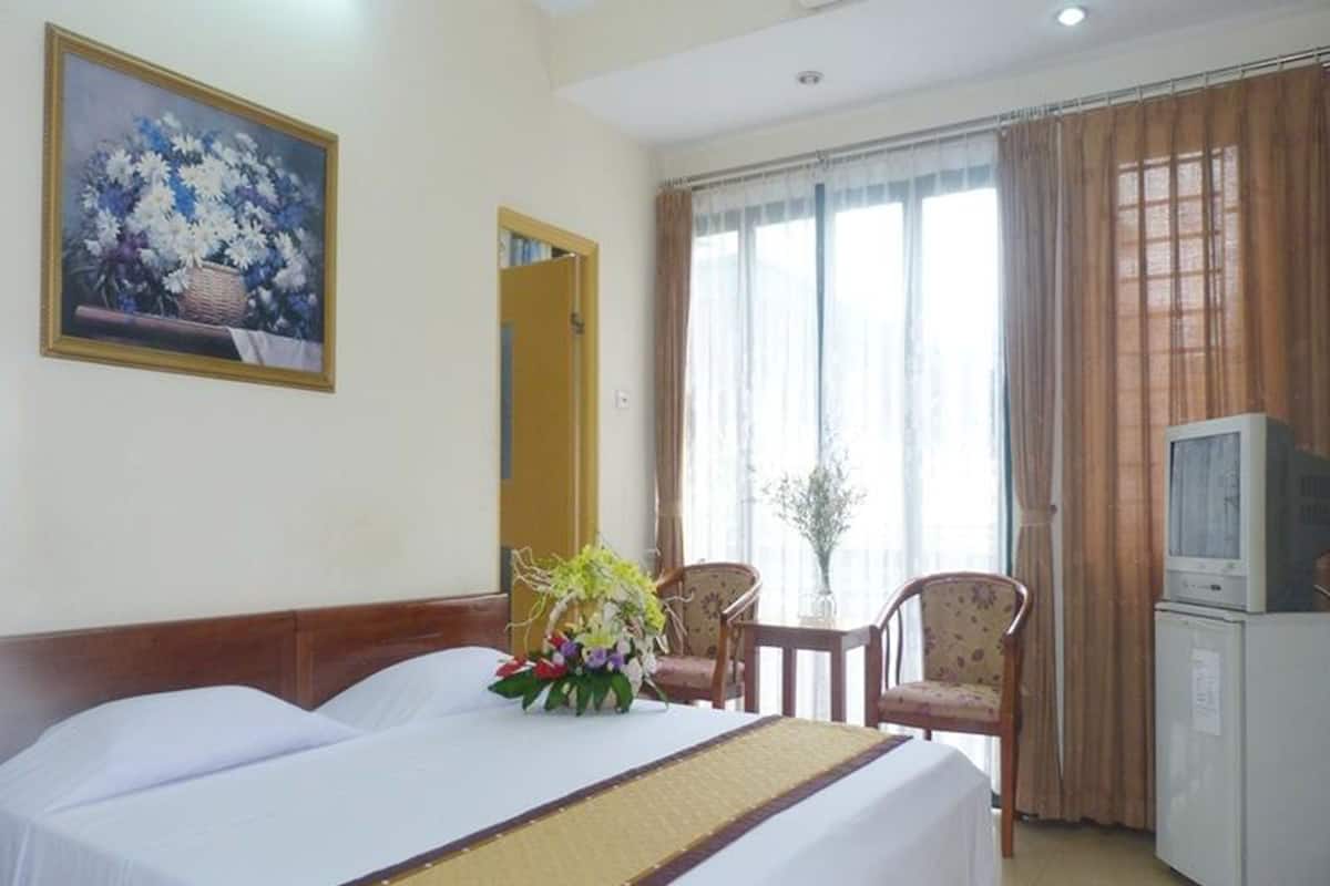 A hotel room with two beds, a television, a small table with chairs, and a painting on the wall.