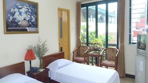 A hotel room with two beds, a painting of flowers, a desk with a lamp, a TV, and a view of the outside.