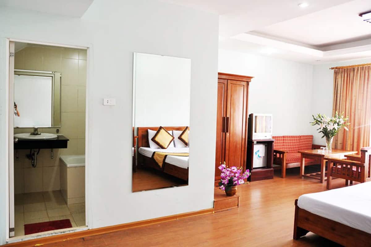 A hotel room with a bed, a desk, a chair, a small table, a mirror, a cabinet, and a bathroom with a sink and toilet.