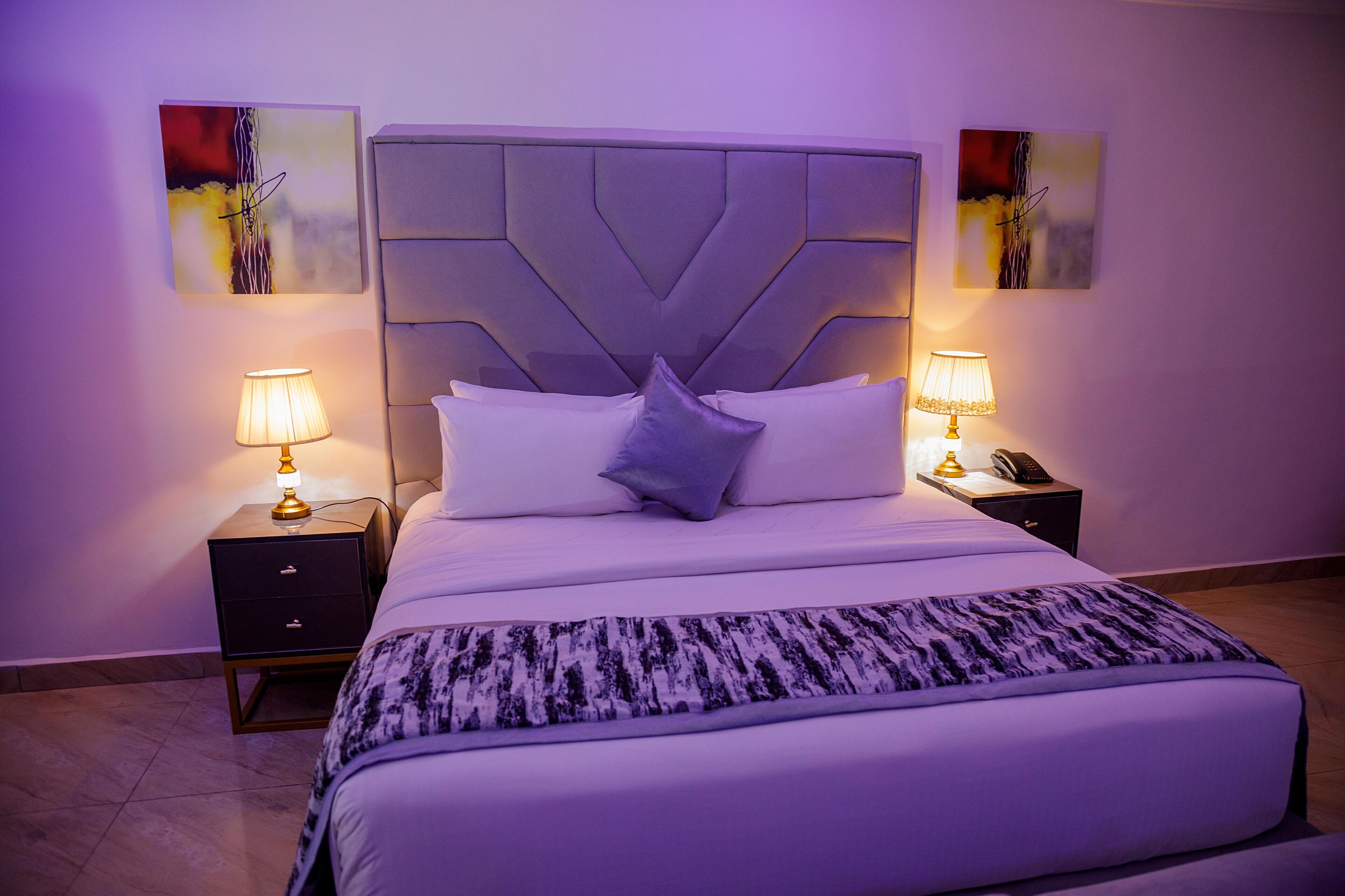 A neatly made bed with a patterned throw, two bedside tables with lamps, and abstract artwork on the walls.