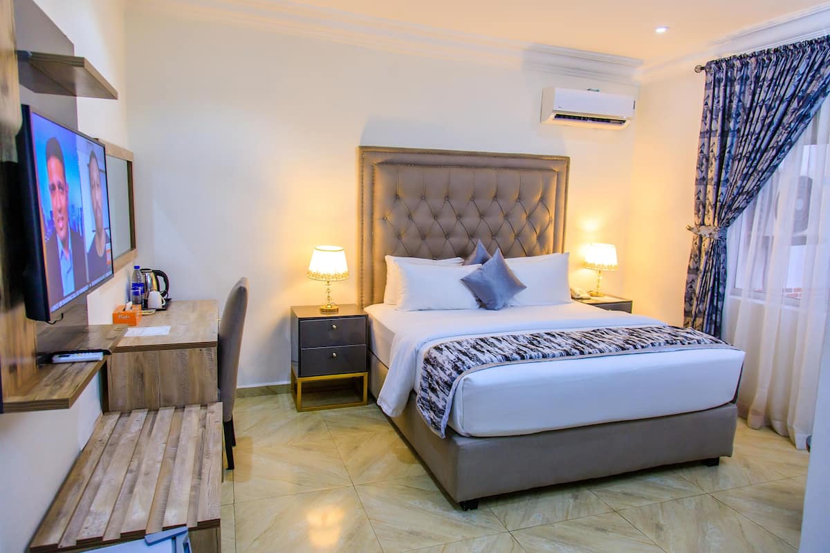 A hotel room with a bed, bedside tables, a desk, and a television.